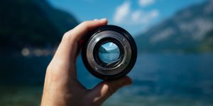 Hand holding a camera lens looking over the water