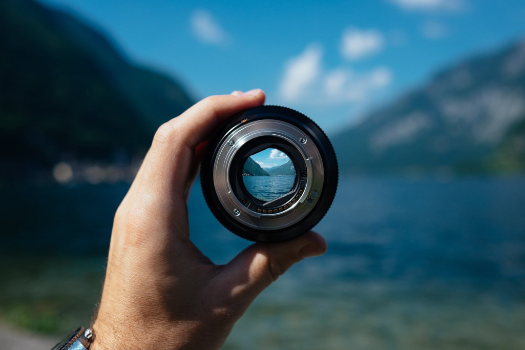 Hand holding a camera lens looking over the water