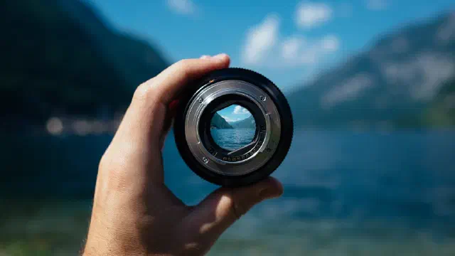 Hand holding a camera lens looking over the water